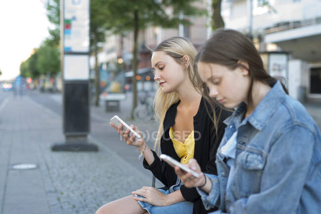Sisters with smart phone sitting in city — Fotografia de Stock