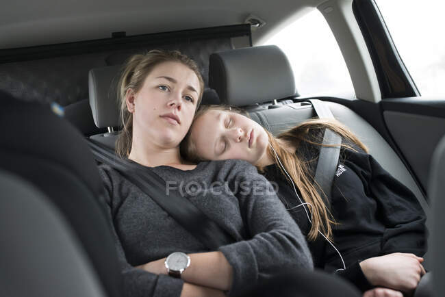 Mujer joven sentada junto a su hermana dormida en el coche - foto de stock