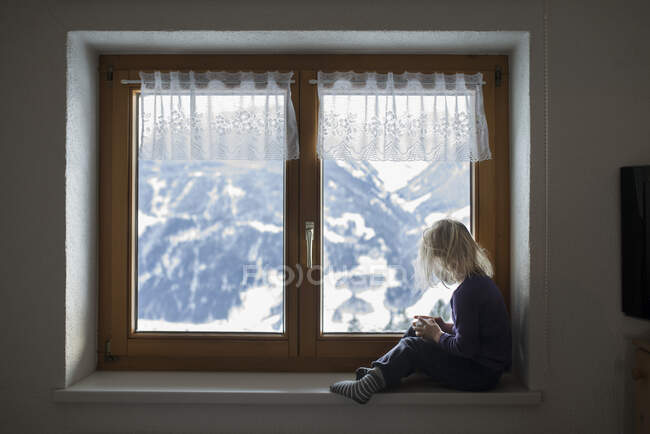 Дівчинка сидить біля вікна в австрійських Альпах. — стокове фото