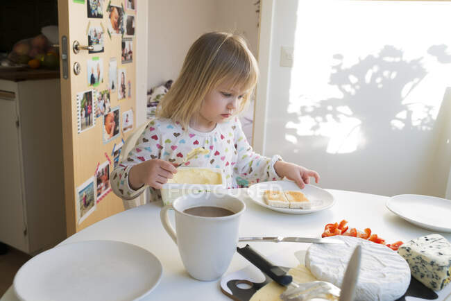 Девушка тосты с маслом за столом — стоковое фото