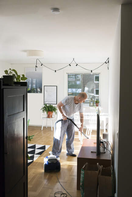 Man using vacuum cleaner in living room — Photo de stock