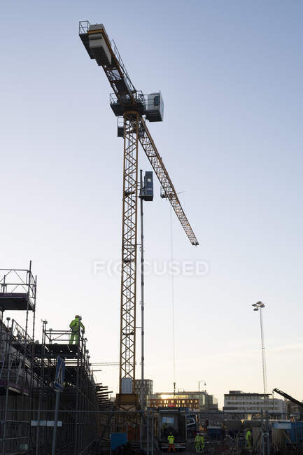 Construction worker standing on scaffolding by crane — Photo de stock