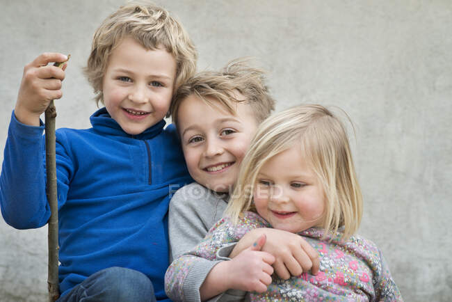 Brothers and sister smiling against gray background — Stock Photo