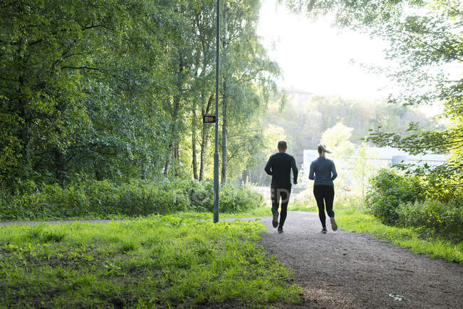 Man and woman jogging on trail in forest - foto de stock