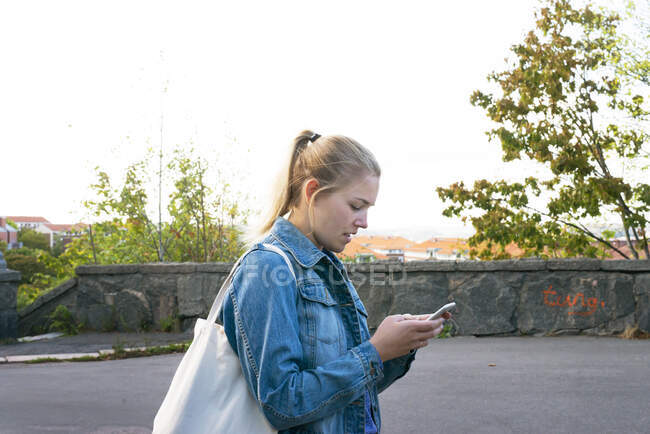 Young woman holding cell phone on road — Stockfoto