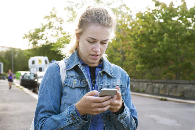 Young woman holding cell phone on road — Stock Photo