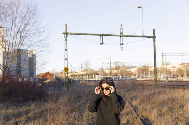 Young woman wearing sunglasses on overgrown railroad tracks — Stock Photo