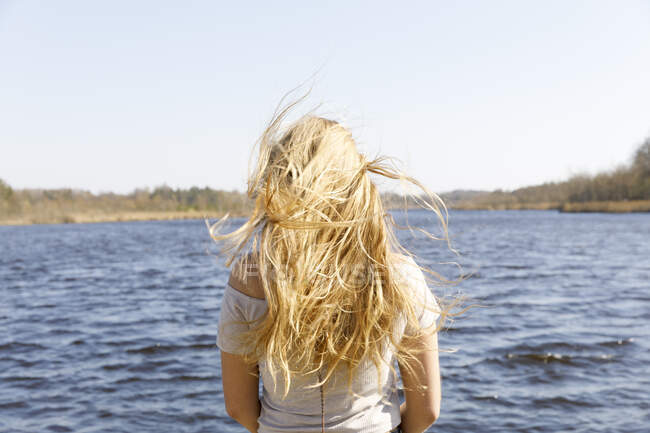 Вид сзади на задутую ветром женщину с светлыми волосами по морю — стоковое фото