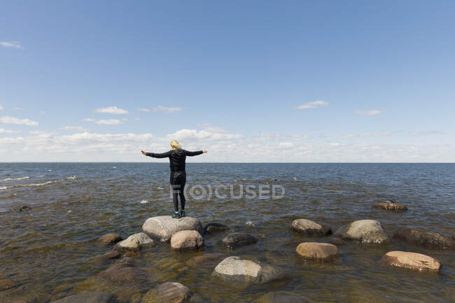 Femme debout les bras tendus sur des rochers dans le lac Vanern, Suède — Photo de stock