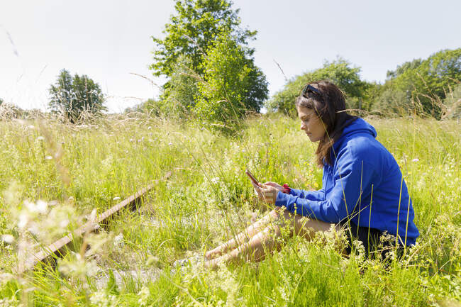Junge Frau benutzt Smartphone während sie im Feld sitzt — Stockfoto