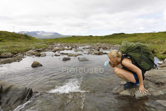 Женщина пьет воду из реки во время похода — стоковое фото