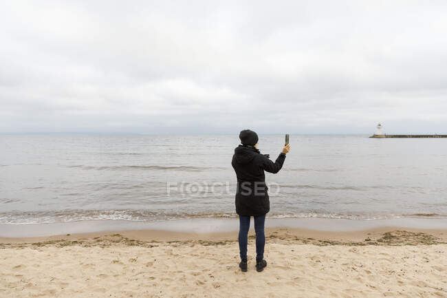 Woman taking photograph with smart phone by lake — Fotografia de Stock