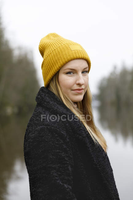 Young woman in yellow beanie by lake — Fotografia de Stock