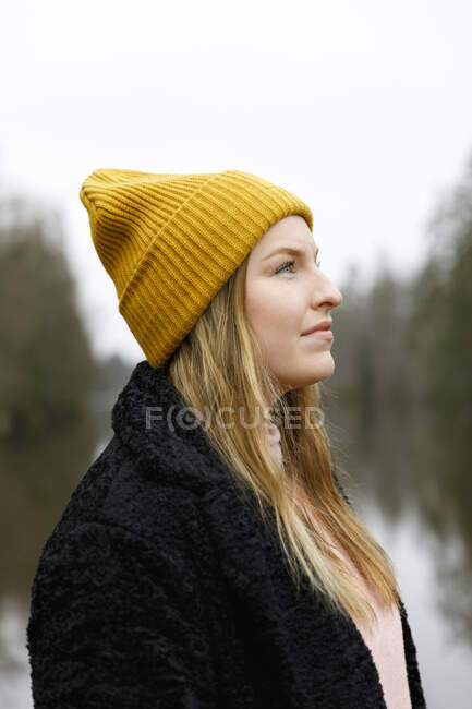Young woman in yellow beanie by lake — Stockfoto