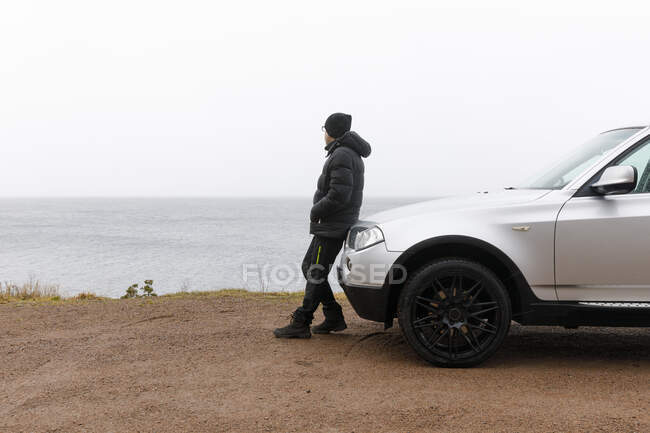 Man leaning on car by lake — Stockfoto
