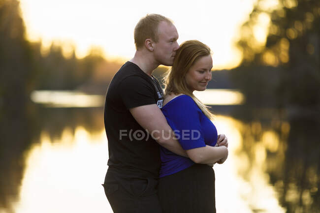 Young couple embracing by lake at sunset — Stock Photo