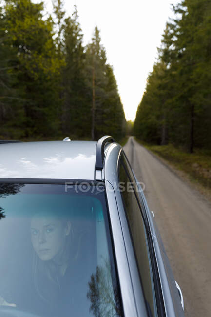 Woman in car on road by forest — Stock Photo