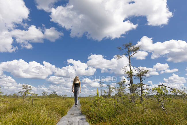 Young woman walking on boardwalk in field — Photo de stock