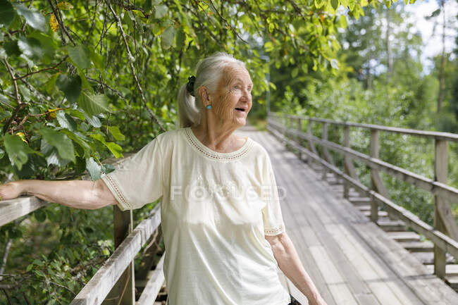 Donna anziana appoggiata su ringhiera di legno di ponte — Foto stock