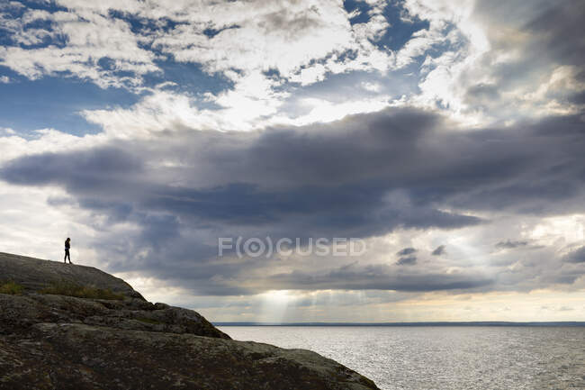 Femme debout sur le rocher par la mer au coucher du soleil — Photo de stock