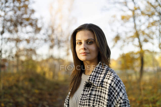Young smiling woman wearing coat in autumn forest - foto de stock