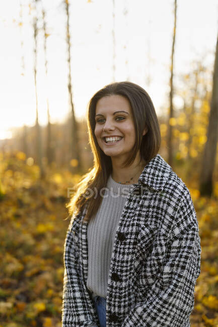 Mujer sonriente joven vistiendo abrigo en bosque de otoño - foto de stock