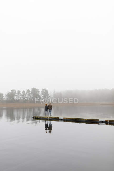 Young man and woman standing on pier at lake — Stockfoto