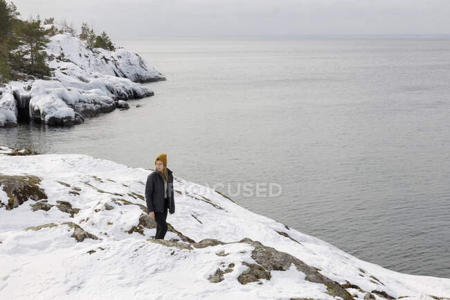 Young woman walking in snow by sea — Foto stock