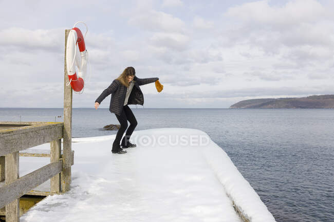 Young woman holding beanie balancing on snowy pier — Photo de stock