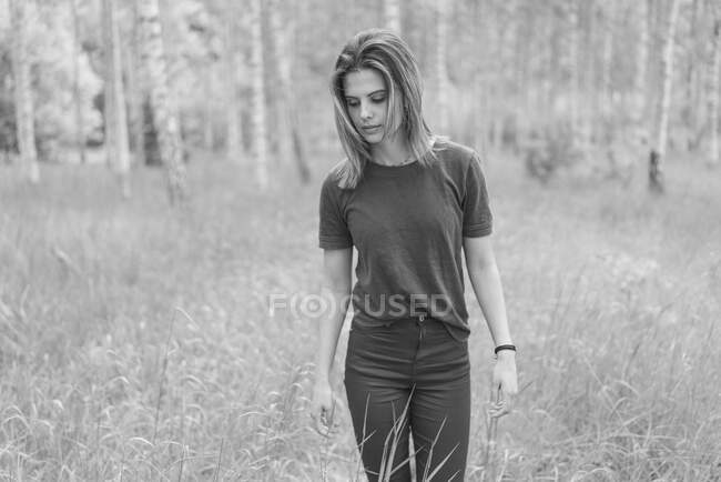 Young woman in field by forest — Stockfoto