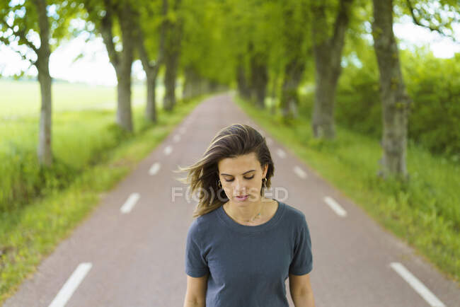 Jeune femme marchant sur la route par les arbres — Photo de stock