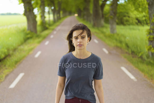 Молодая женщина, идущая по дороге у деревьев — стоковое фото