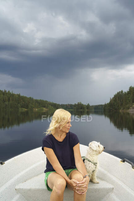 Woman and dog sitting in boat on lake — Foto stock