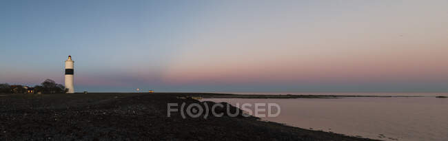Lighthouse on coast at sunset - foto de stock