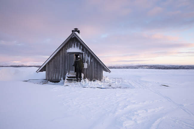 Женщина входит в бревенчатую хижину зимой в Рогенском заповеднике, Швеция — стоковое фото