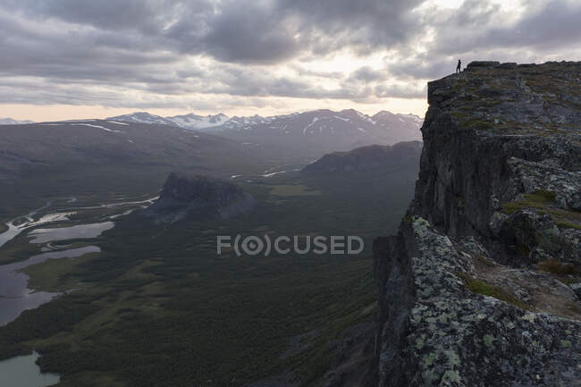 Mujer distante de pie en el acantilado sobre el valle de Rapa en el Parque Nacional Sarek, Suecia - foto de stock