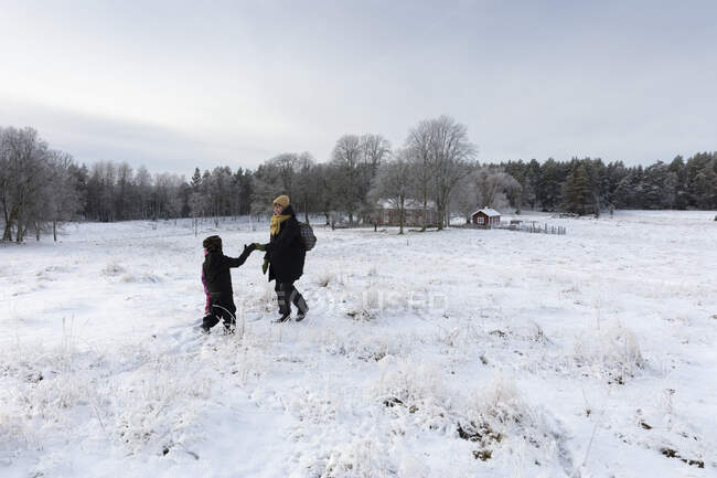 Мать и сын держатся за руки в снежном поле — стоковое фото