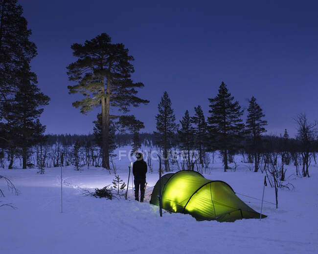 Giovane donna in piedi vicino alla tenda nella foresta innevata di notte — Foto stock