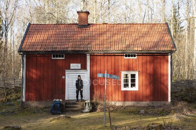 Young woman standing outside red cabin in forest — Photo de stock