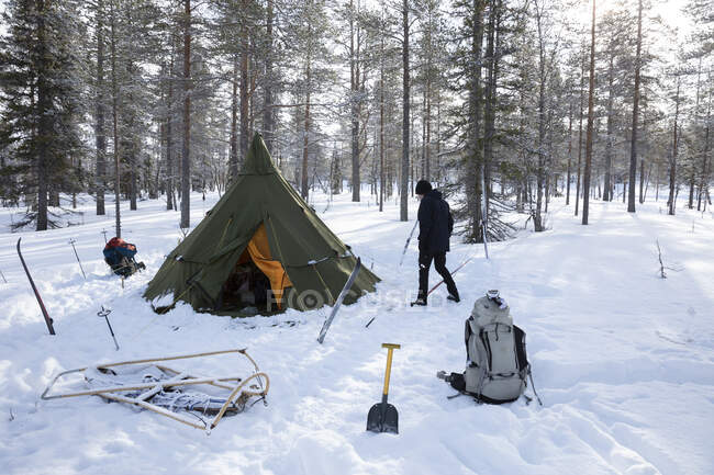 Young man walking by tent in snowy forest — Foto stock