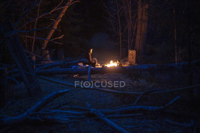 Young woman sitting by campfire in forest at night — Foto stock