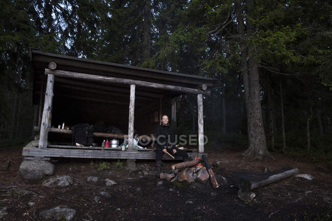 Young woman sitting in log cabin by campfire — Fotografia de Stock