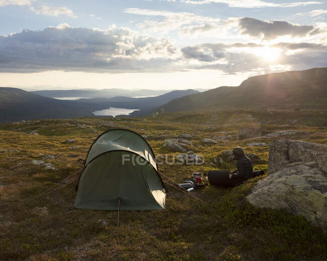 Young woman sitting by tent in field — Fotografia de Stock