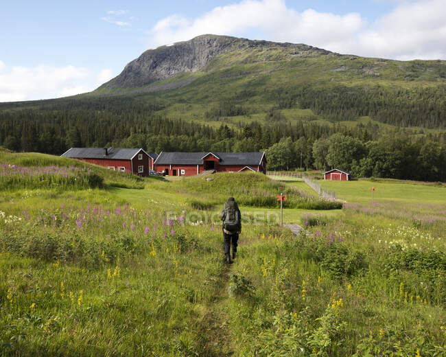 Jeune femme randonnée dans le champ par les maisons et la montagne — Photo de stock