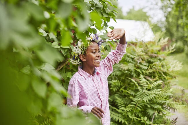 Усміхнений хлопчик у квітковій короні під деревом — стокове фото