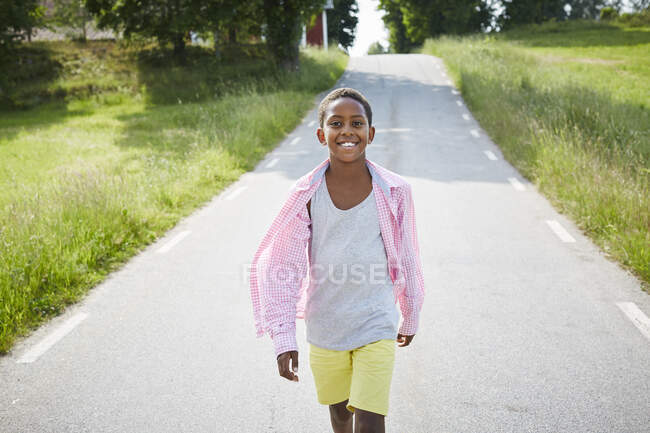 Garçon en chemise rose marchant sur la route — Photo de stock