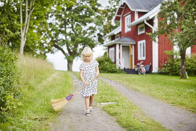 Girl sweeping driveway in summer — Stockfoto