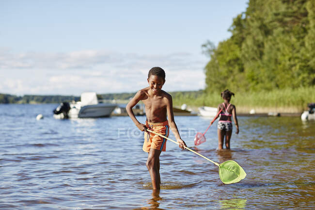 Siblings playing with nets in lake — Stockfoto