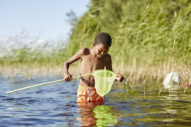Boy playing with net on lake — Stockfoto