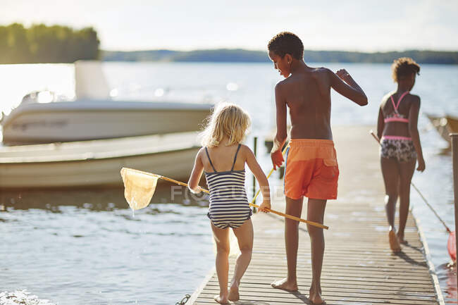 Siblings playing with nets on lake jetty — Stock Photo